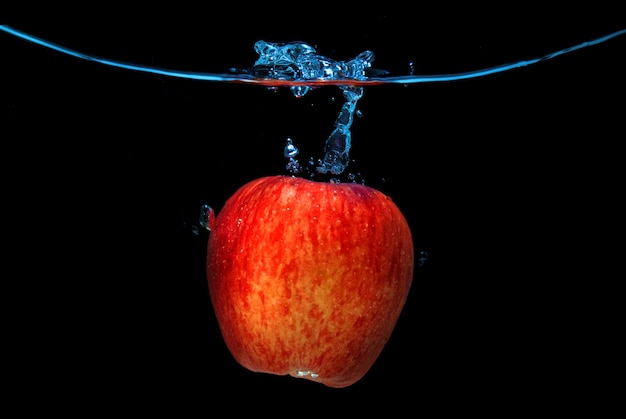 Foto la mela rossa è caduta in acqua con spruzzata isolata sul nero