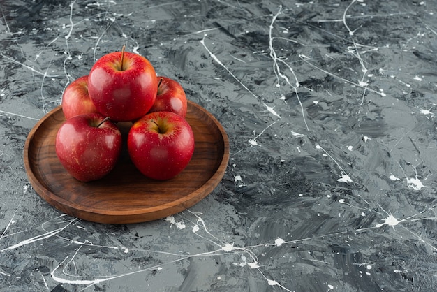 Red apple fruits placed on a round wooden plate.