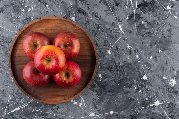 Red apple fruits placed on a round wooden plate.