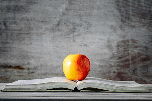 Red apple on open book with wooden background