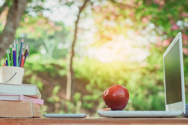 A red apple and pencil sitting on laptop keyboard with school books 