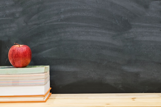 Photo red apple resting on the book with black board background, back to school concept.