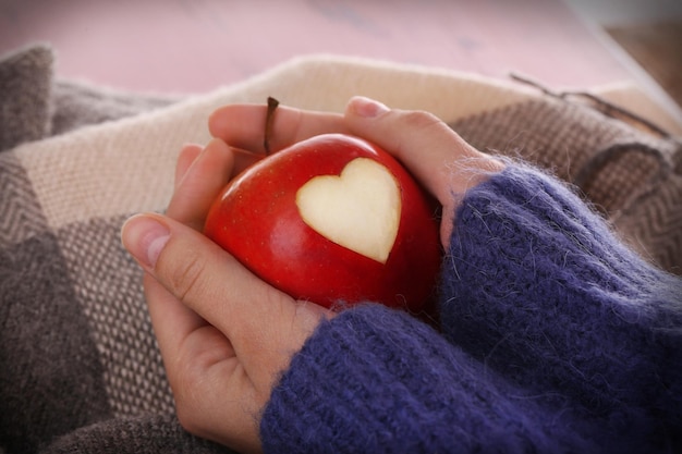 Красное яблоко с сердцем в женских руках крупным планом