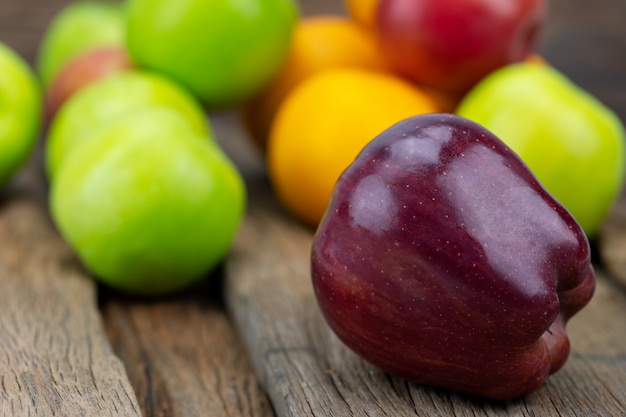 Foto le mele rosse sono disposte su un pavimento di legno con uno sfondo sfocato e altri frutti.