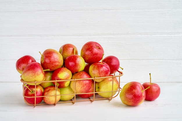 Red apples in basket on white wooden background. Copy space