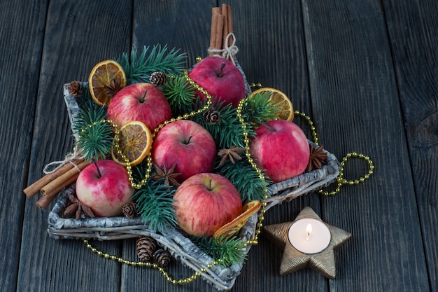 Red apples, cinnamon, pine branches, gold beads and a candlestick with a candle