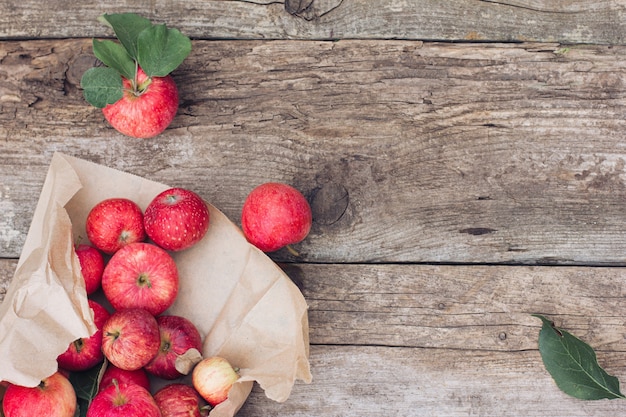 Le mele rosse giacciono su un fondo di legno rustico in un sacchetto di carta strappato. imballaggio ecologico. il raccolto del contadino, il raccolto autunnale