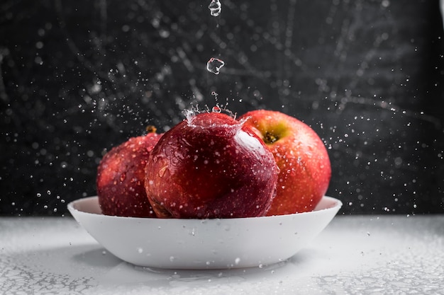 Red apples in a plate of water drops