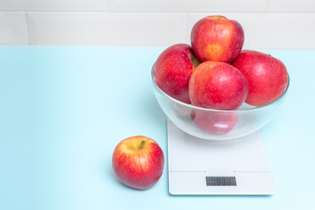 Red apples in a transparent bowl on a kitchen scale, copy space, closeup