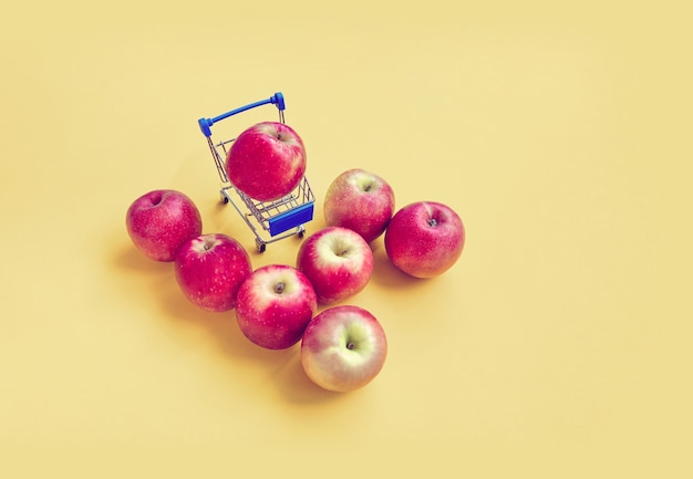 Red apples with mini shopping cart with yellow vintage color theme