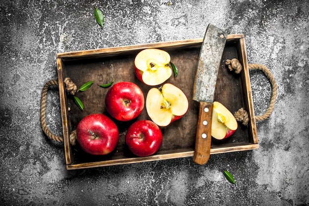 Red apples with old knife on tray on rustic table.