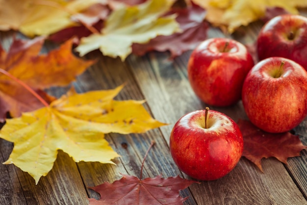 Красные осенние яблоки с кленовыми листьями на деревянном столе