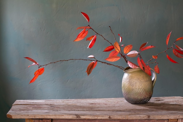 Red autumn leaves in ceramic jug on old wooden table