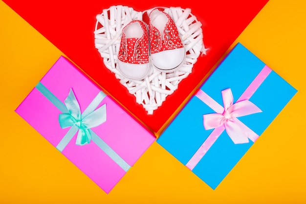 Red baby shoes with white polka dots on a red background with gifts