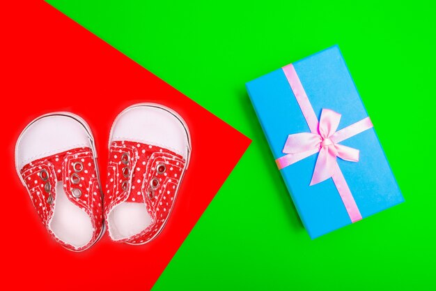 Red baby shoes with white polka dots on a red background with gifts