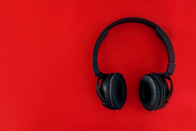 On a red background are black headphones. Flat lay.