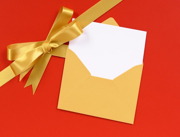 red background gold christmas gift ribbon bow with blank invitation or greetings card diagonal
