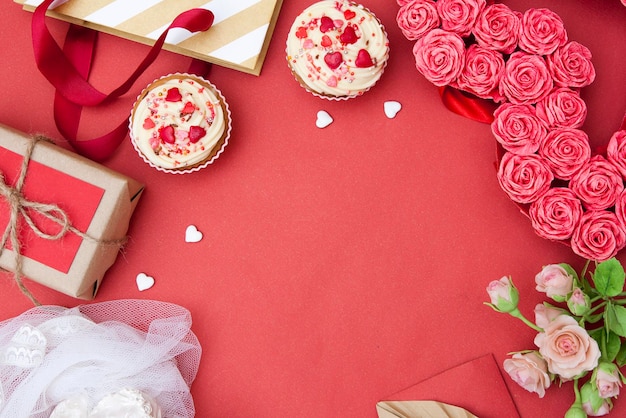 Красный фон с кексами, сердечками, подарками, цветами. Свободное место для текста поздравления с днем святого валентина