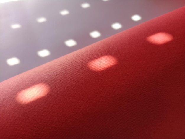 물방울 무늬가 있는 빨간색 배경 블라인드의 구멍을 통해 빛나는 태양 광선과 색상 표면에 밝은 흐릿한 원을 그리는