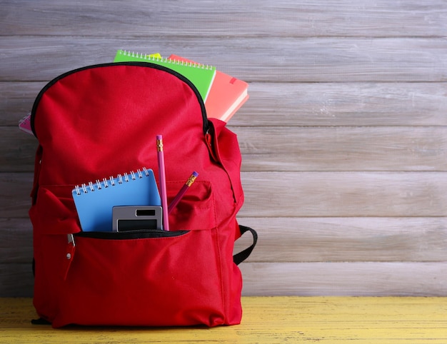 Foto borsa rossa con materiale scolastico su fondo di legno