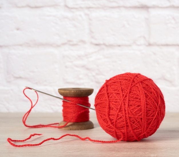 Red ball with woolen thread and large needle on white brick wall background