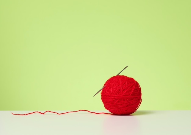 Red ball with woolen thread on white table, green background