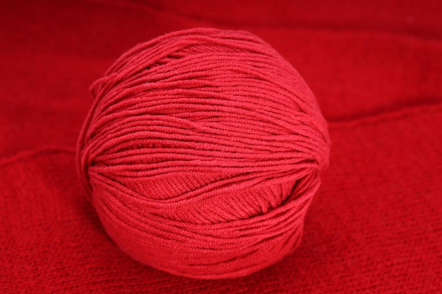 На вязанной скатерти лежит красный клубок шерсти. Фото высокого качества