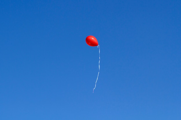 A red balloon flying up in the blue sky