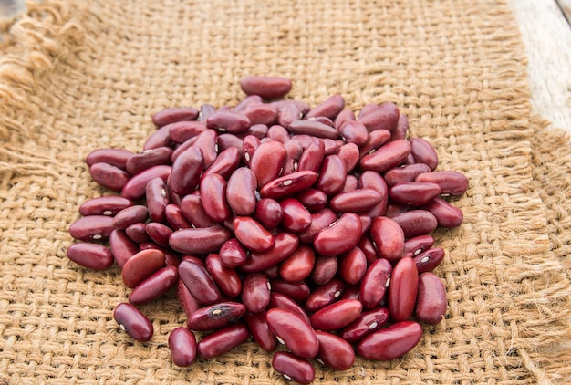 Red beans in burlap sack on wooden background