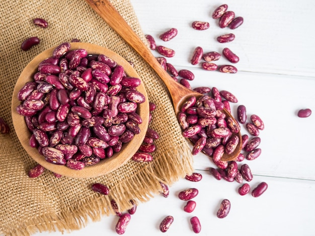 Red beans close-up on a wooden spoon on a white wooden table, copy space