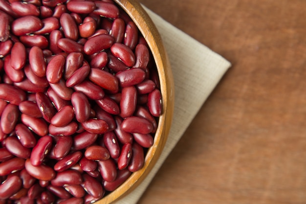 Red beans in wooden bowl putting on linen and wooden background.