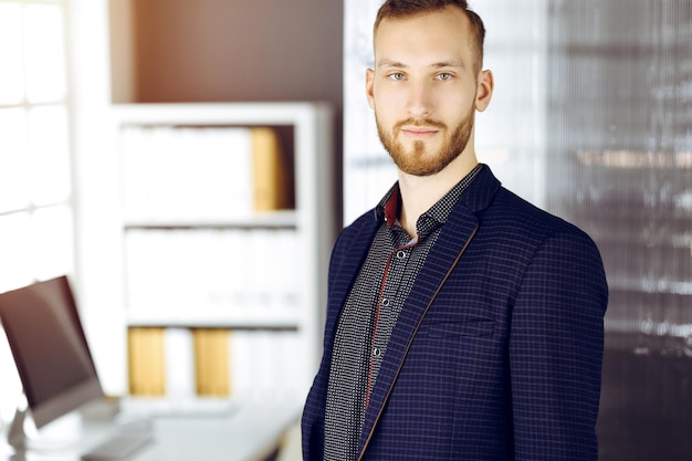 Photo red-bearded friendly adult businessman looking at camera. business headshot or portrait in sunny office.