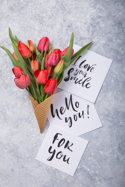 Red  beautiful tulips in an ice cream waffle cone with card Hello you on a concrete background. Conceptual idea of a flower gift. Spring mood