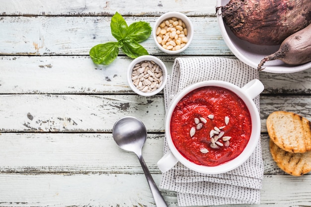 Photo red beetroot mashed soup with cream and sunflower seeds in a white bowl, top view