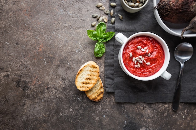 red beetroot mashed soup with cream and sunflower seeds in a white bowl, top view