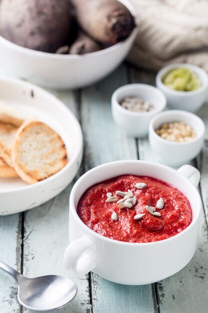 Red Beetroot mashed soup with cream and sunflower seeds in a white bowl.