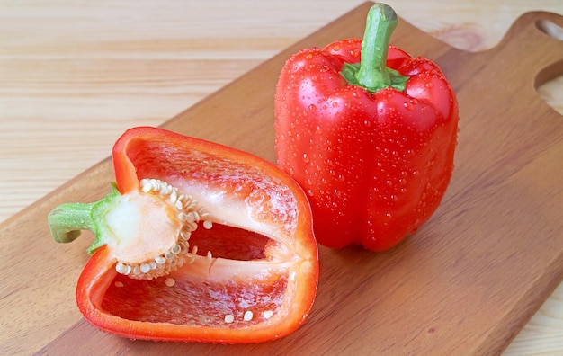 Red bell peppers with water droplets on wooden cutting board