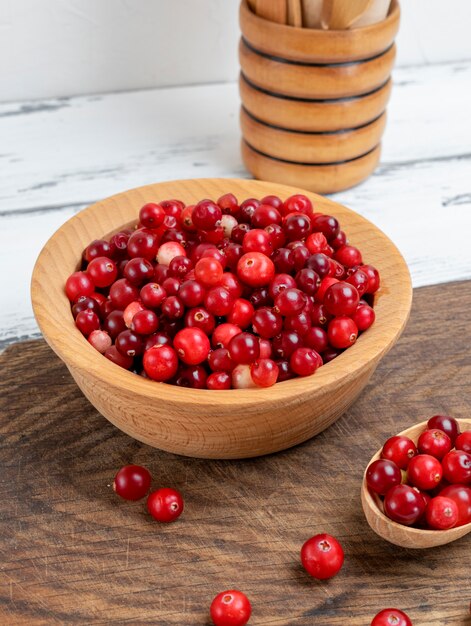 Red berries of ripe lingonberries in a wooden bowl on a white table