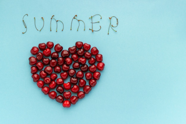 Photo red berry cherries shape heart and text summer on blue background copy space