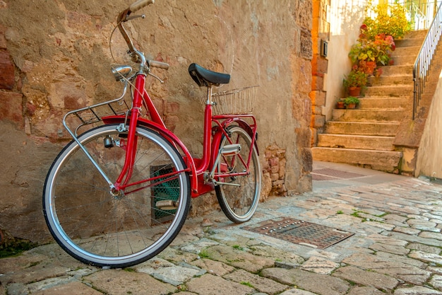 A red bicycle stands on the narrow street of the old city near the stone wall of the building