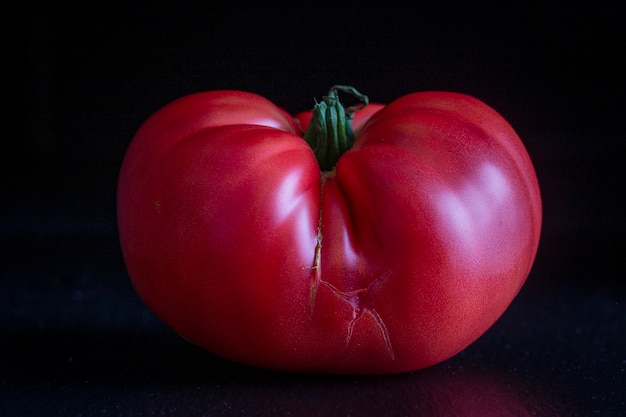 Red big cracked tomato on black background, close up