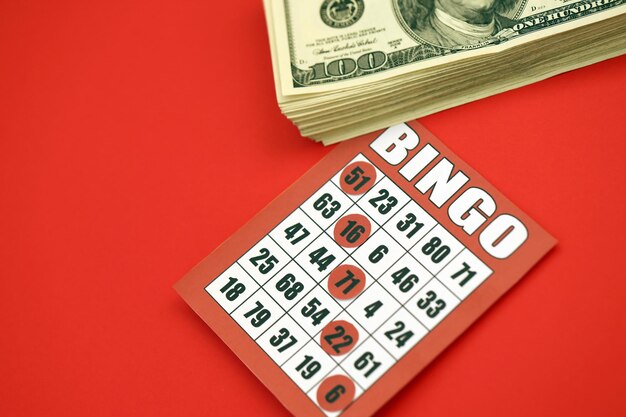 Scheda bingo rossa o carta da gioco per fiches vincenti e pila di banconote da un dollaro classico americano o canadese da cinque a cinque carte da bingo su sfondo rosso