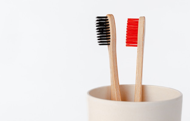 Red and black bamboo toothbrushes in eco cup. Copy space, close up.