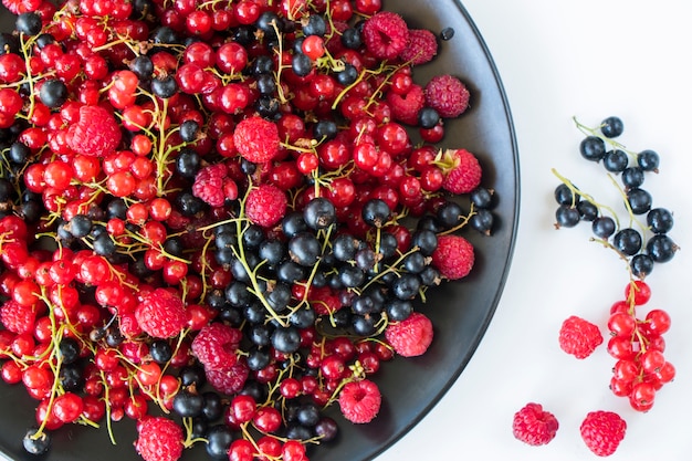 Red and black currant and loganberries on the black plate and white background. Large group of colorful berries.