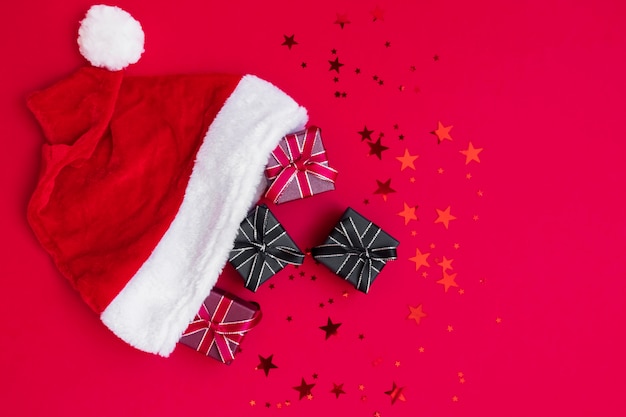 Scatole regalo rosso, nero piccolo regalo in cappello di babbo natale su sfondo rosso intenso