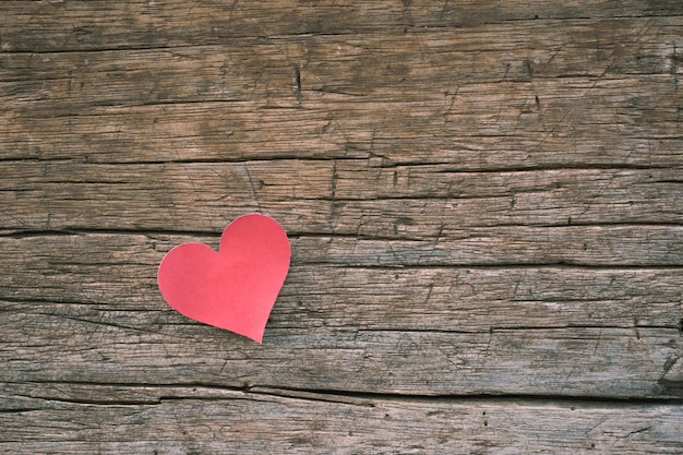 Red blank paper note with heart shape on grunge wooden background