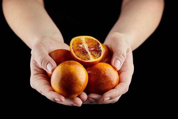 Red or blood oranges in hands on black