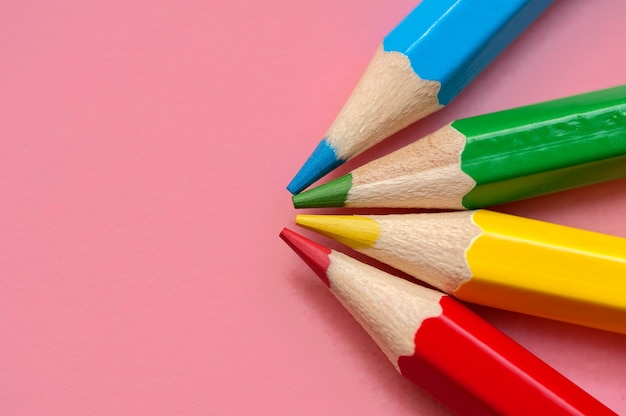 Red blue green and yellow pencils on a pink background