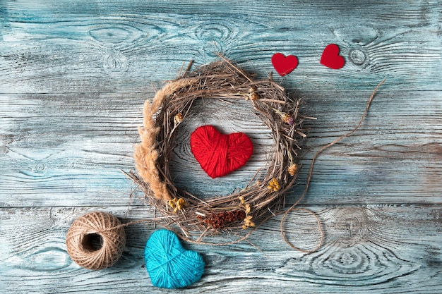 Red and blue hearts and a wreath of natural branches and dry grass on a gray-blue wooden background.