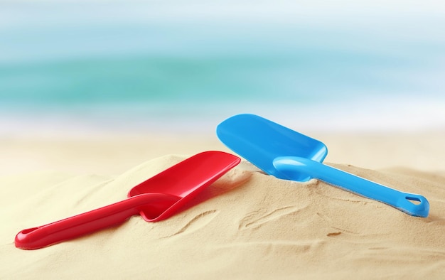 Red and blue plastic toy shovels on sandy beach near sea